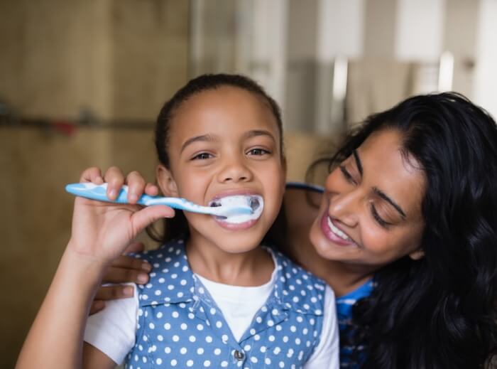 Mother teaching child how to brush her teeth