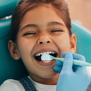 Child smiling while dentist looks at their teeth with dental mirror