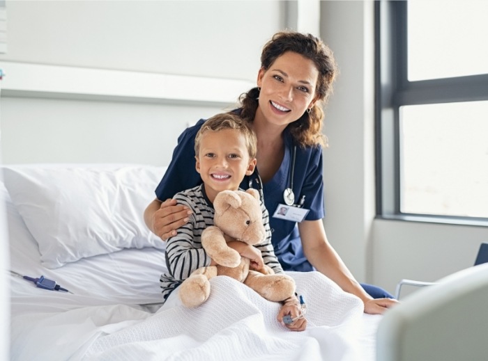 Child smiling in hospital bed after general anesthesia dental treatment