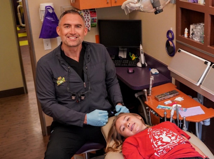 Pediatric dentist and dental patient smiling after refreshing teeth cleaning