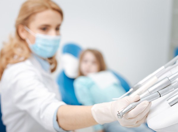 Dentist reaching for instrument with child in the background
