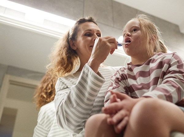 Mom helping daughter brush her teeth at home